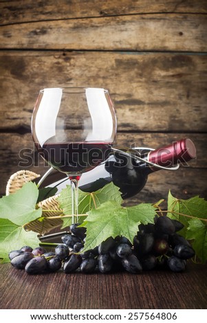 Winery background. Wineglass with bottle of red wine and cluster of grape on wooden table