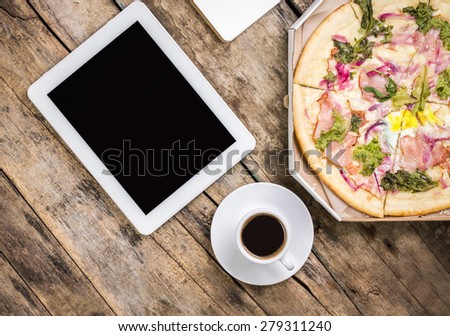 Coffee break background. Workplace mock-up with digital tablet and cup of coffee with pizza in box on old wooden background. Top view image
