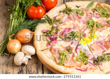 Gourmet pizza with ingredients around. Sliced pizza with onion, tomato and herbs on wooden table.
