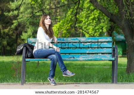 Young beautiful woman sitting on bench in park. Pretty girl at outdoors on summer day. Nature environment background.