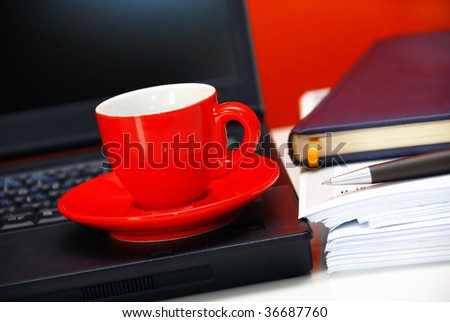 red cup over black notebook on office desk still life