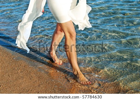 legs of woman in white dress walking on beach by blue sea water