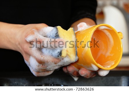 hands with sponge washing dishes in kitchen sink