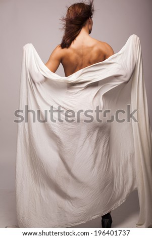 Sexy brunette woman with perfect body covered with white transparent textile on gray isolated background