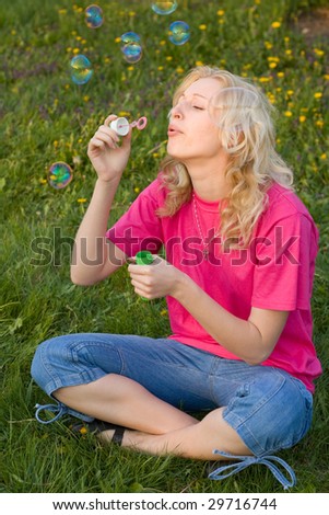 blonde girl makes soap bubble on a grass
