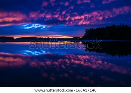 Beautiful silhouette of a sunset in Tofino, British Columbia reflection off the calm cove split in half by a distant island.