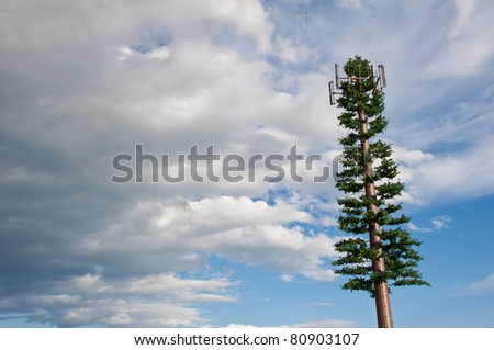 Cellular telephone tower disguised as a tree with bright blue sky & clouds behind it