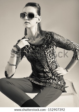 Black and white portrait of Vogue style beautiful young woman in sunglasses sitting cube in studio