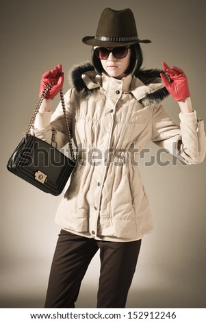 Shot of an attractive fashionable girl in jacket with sunglasses, bag posing gold background