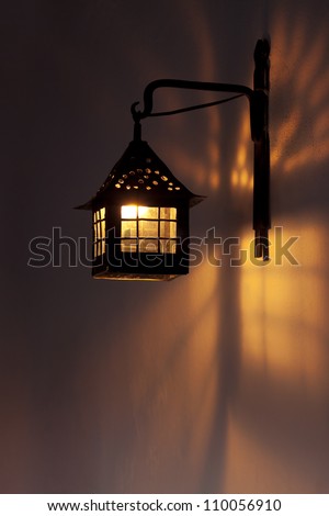 Antique wall lamp glowing orange in the night. Lights and shades patterns on the wall.
