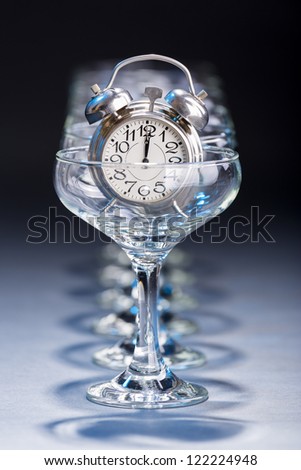 Alarm clock in an empty champagne glass showing twelve o\'clock hour.