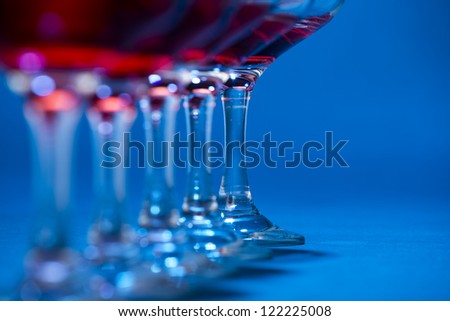 Detail of glasses filled with red wine over blue background.