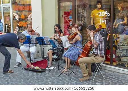 BRASOV, ROMANIA - JULY 14: Unidentified string quartet artists receive money rewards for their performance from tourists on July 14, 2013 in Brasov, Romania.