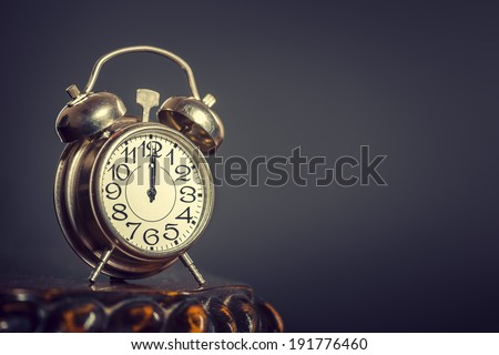 Old alarm clock showing twelve o'clock over dark background.