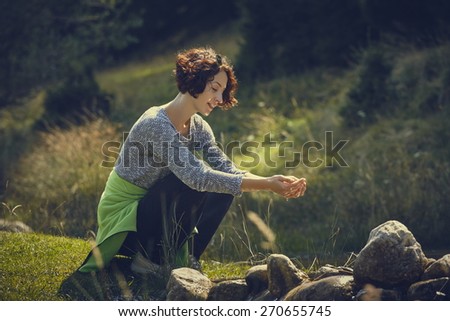 Smiling young hiking lady washing her hands in the fresh cool water of a mountain stream on a sunny summer day.
