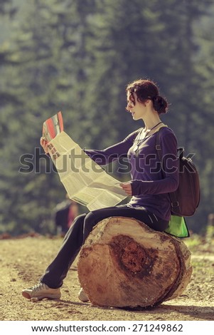Hiking young lady resting on a stump and reading a travel map on a sunny day.