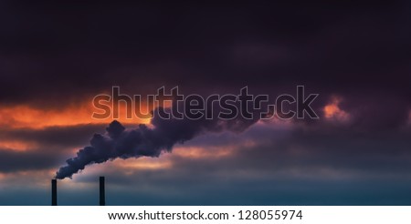 Heavy smoke spewed from coal powered plant smoke stacks under dramatic cloudy evening sky