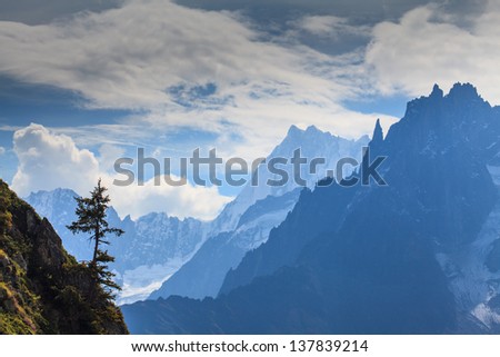 Snow covered mountains, rocky cliffs and an isolated pine tree in the French Alps