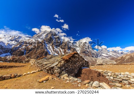 Snow covered mountains, rocky peaks and stone lodge in Himalaya
