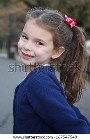 Little girl in an urban setting smiles at the camera. Beautiful girl with long hair tails of.