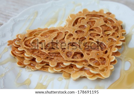 Stack of Small pancakes in syrup on white background. Lace heart-shaped pancakes with honey. Food style.