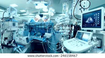In advanced operating room with lots of equipment, patient and working surgical specialists