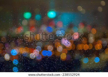 Blurred skyline lights with bokeh effect seen behind a wet window with raindrops.
