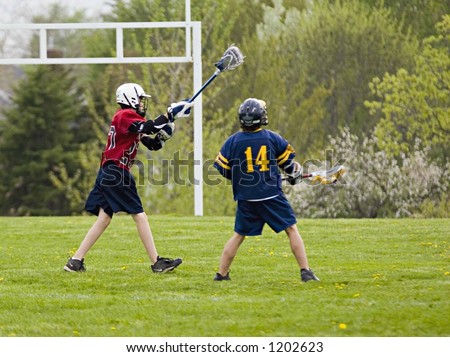 Color DSLR picture of two boys playing lacrosse on a green field.  The sport is fast paced and action packed.  Horizontal image with copy space for text.