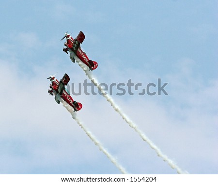 Color DSLR picture of two red stunt planes against a blue sky.  Speeding airplanes are trailing white smoke contrails.  Dangerous and fast. Horizontal orientation with copy space for text.