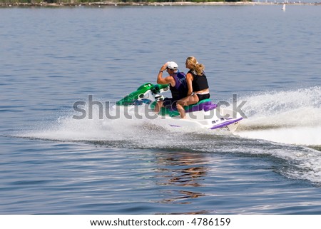 Color DSLR image of a couple of people, man and woman, on a jet-ski speeding across the calm salt water bay. From behind. Horizontal with copy space for text.