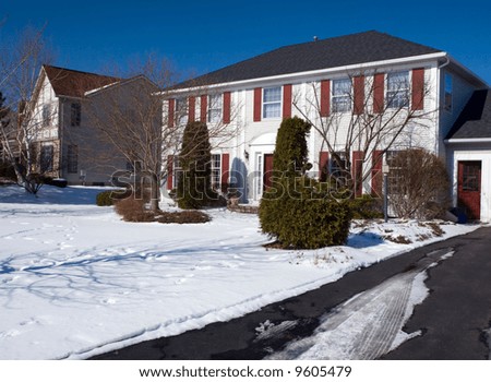 Color DSLR image of suburban center hall colonial house in the winter time, with snow in the yard and a blue sky background. Horizontal with copy space for text.