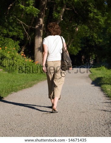 Color DSLR picture of a fit mature, adult woman walking on a path, from behind.  The brunnette is wearing tan khakies and a white shirt.  Vertical orientation with copy space for text.