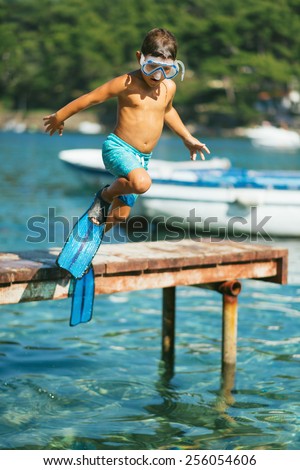 Portrait of a beautiful sun tanned boy jumping into clear blue sea with a mask and flippers and boats in the background
