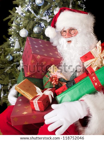 Sitting santa claus sitting in front of the christmas tree with gifts