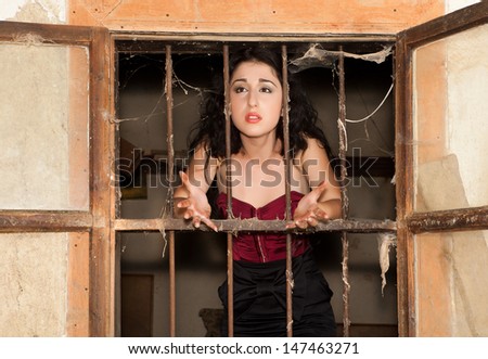 Young woman behind bars of a derelict building