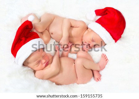 Twin babies lying hand in hand with santa christmas hats