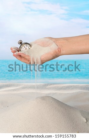 Hand with pocket watch and sand flowing on the beach