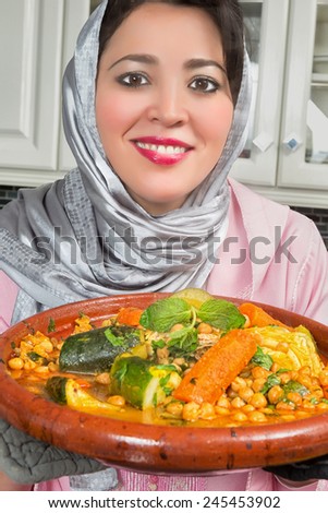 Smiling Moroccan immigrant woman in Europe presenting her tajine dish during Ramadan in her modern kitchen