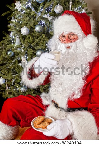 Santa claus in front of a christmas tree eating cookies and milk