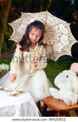 Girl dressed as Alice in Wonderland girl drinking tea with a white rabbit