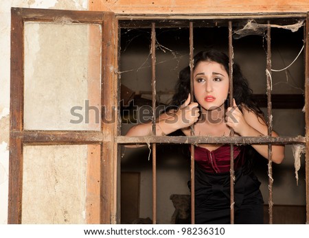 Sad woman in prison behind bars of a derelict building