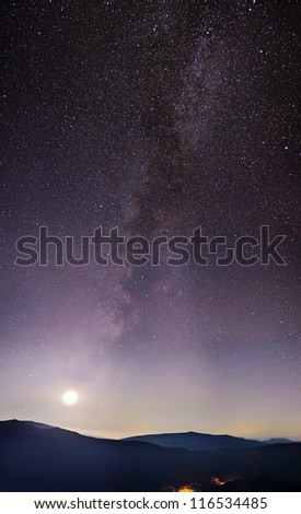 Part of a night sky with stars and Milky Way on with Moon and mountains below