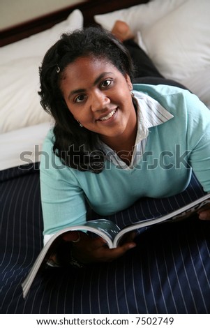 A woman reads a magazine while sitting on a bed