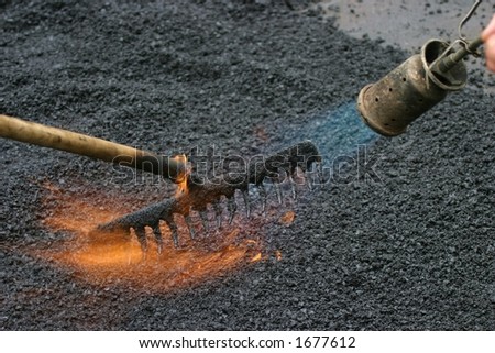 Workers preparing a road for a new tar layer by using a gas burner and rake