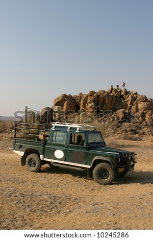Expedition vehicle parking in the namibian bushland with 3 team members standing on a lookout hill in the background