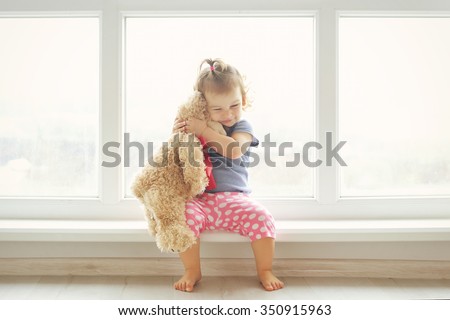 Adorable little girl hugging a teddy bear. Cute baby at home in white room is sitting near window.  商業照片 © 