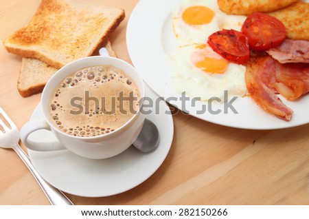 A set of traditional English breakfast, Plate with fried eggs, bacon and hash-brown, toast and coffee on wooden table