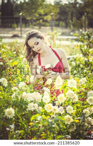 Beautiful young woman  in a garden of roses at sunny summer day