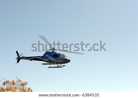 Helicopter flying over tree level, clear sky.