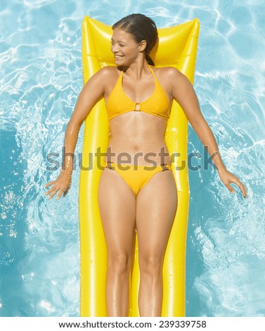 Young pretty woman with perfect tanned body lying on yellow air mattress in the pool